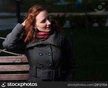 redhead 20s women sitting on bench outdoor in autumn park, weared scarf and coat