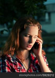 Redhead girl calling by mobile phone outdoors serious face. Toned image.