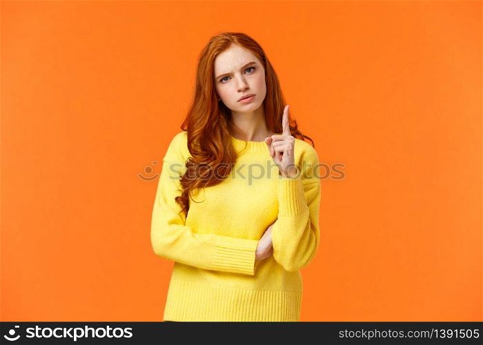 Redhead girl express disapproval as shaking her finger at someone with disappointed angry face, frowning give warning, prohibit unacceptable behaviour, standing displeased orange background.. Redhead girl express disapproval as shaking her finger at someone with disappointed angry face, frowning give warning, prohibit unacceptable behaviour, standing displeased orange background