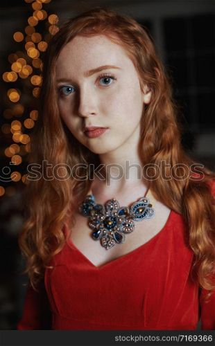 Redhead teenager in a red dress and an ornate necklace looking at the camera