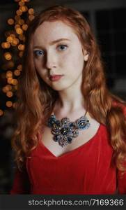 Redhead teenager in a red dress and an ornate necklace looking at the camera