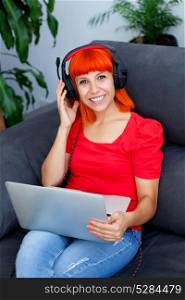 Redhead woman in red listening music with a laptop at home