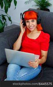Redhead woman in red listening music with a laptop at home