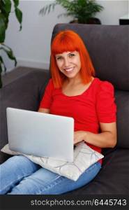 Redhead woman in red with a laptop at home