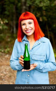 Redhead woman in the countryside toasting with a green bottle in the countryside