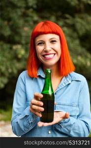 Redhead woman in the countryside toasting with a green bottle in the countryside