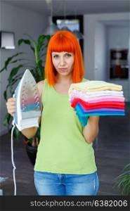 Redhead woman looking at camera and smiling while ironing clothes at home