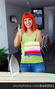 Redhead woman looking at camera and smiling while ironing clothes at home