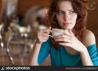 Redhead women sitting in the cafee and holding cup of coffee in the hands looking away