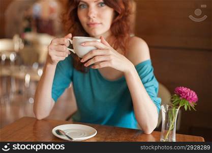 Redhead women sitting in the cafee and holding cup of coffee in the hands looking at camera