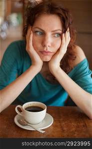 Redhead women sitting in the cafee with cup of coffee on the table befor and looking at camera
