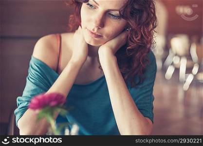 Redhead women sitting in the cafee with pink flower on the table befor and looking at camera and smiling toned image, vintage look