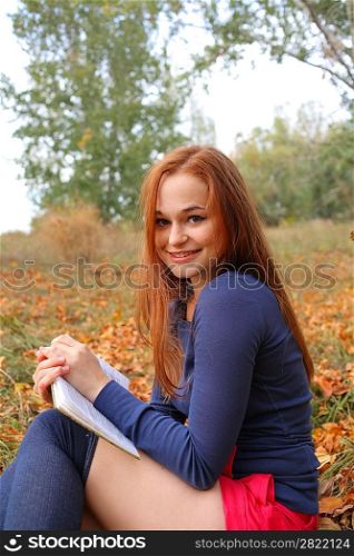 redhead young woman outdoors in the field reading in autumn park