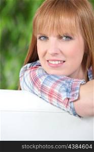 Redheaded woman leaning on the back of a white sofa