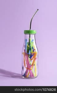 Reduce plastic pollution concept with a reusable metal straw in a glass bottle full of colorful plastic, on purple paper. Eco-friendly drinking straw.