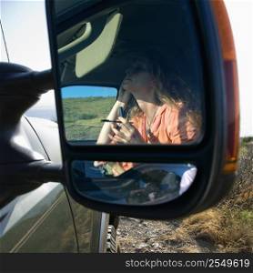 Reflection in vehicle side mirror of Caucasian woman applying mascara.