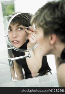 Reflection of a mature woman tweezing her eyebrows in a mirror