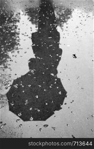 reflection of a woman with an umbrella on wet pavement during rain. Black and white. Vertical view