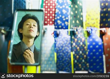 Reflection of a young man adjusting his tie in the mirror of a tie shop
