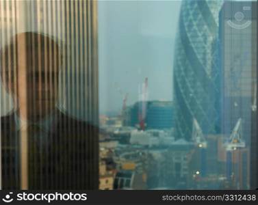 reflection of business man in window with view of London city district in background