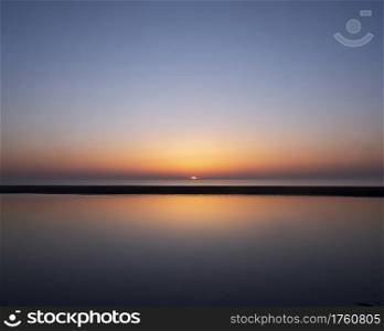 reflection of colorful sunset in water near beach on the dutch coast in holland