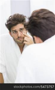 Reflection of ill man examining eyes in mirror