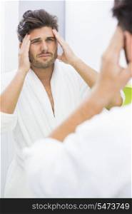 Reflection of man in bathrobe suffering from headache