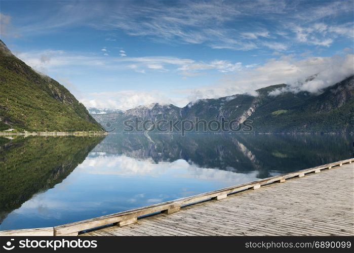 reflection of mountains in fjord in norway with wooden walking track in front