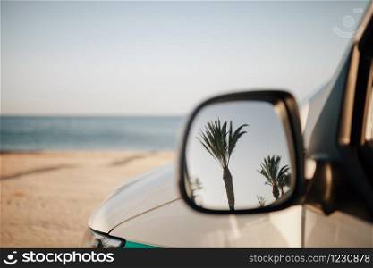 Reflection of palm trees in van outside mirror on the beach