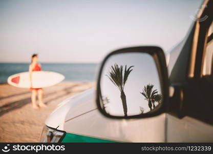 Reflection of palm trees in van outside mirror on the beach