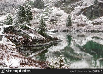Reflection of peaks in mountain lake. Snowy winter in mountain valley