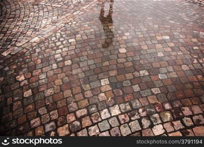 reflection of person in street with cobble stones and puddle after rain