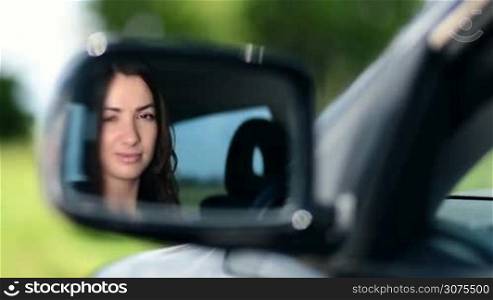 Reflection of pretty smiling brunette woman in the car side-view mirror before the trip