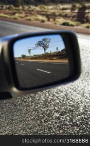 Reflection of rural Australian in rearview mirror of vehicle traveling down two lane asphalt road.