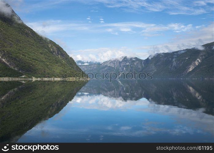 reflection of the mountains in the geirangerfjord in norway with blue water and sky