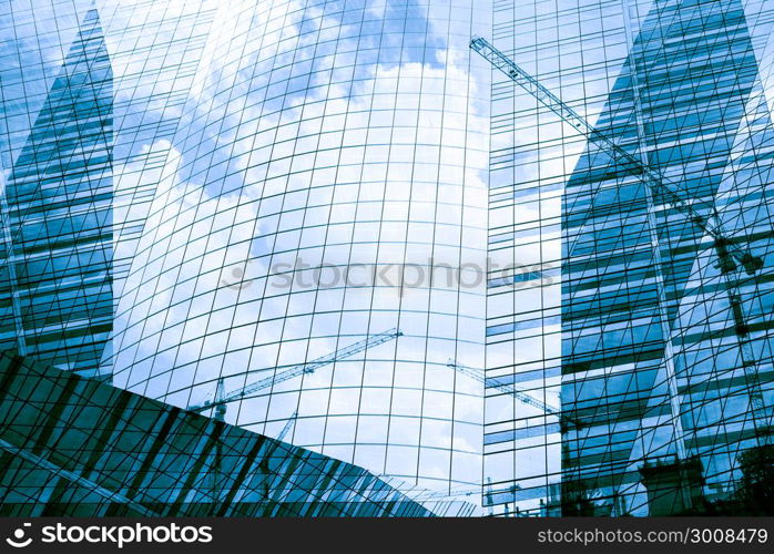 Reflection of tower cranes building construction on building mirror. Abstract background.