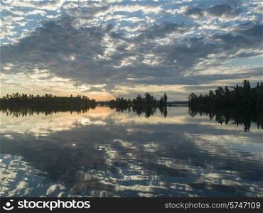 Reflection of trees and clouds on water at dusk, Lake of The Woods, Ontario, Canada