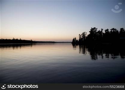 Reflection of trees in water at dusk, Kenora, Lake of The Woods, Ontario, Canada