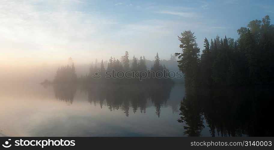 Reflection of trees in water during fog, Lake of the Woods, Ontario, Canada