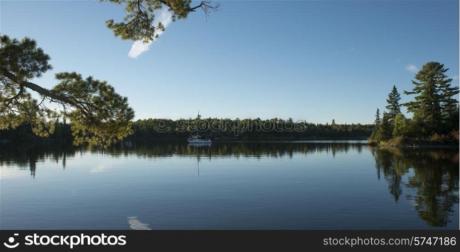 Reflection of trees with a sail boat, Kenora, Lake of The Woods, Ontario, Canada