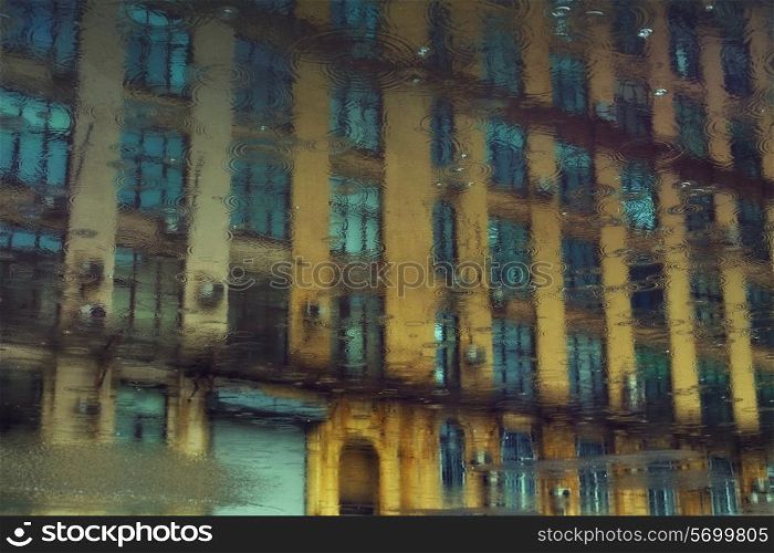 Reflection of urban building in a puddle of rain with the drops