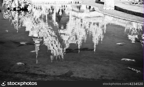 Reflection of white temple Wat Rong Khun in a pond with fishes. Wat Rong Khun is a contemporary unconventional Buddhist temple in Chiang Rai, Chiangmai province, Thailand. It is designed in white color.