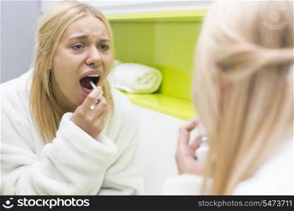 Reflection of woman spraying medicine in mouth