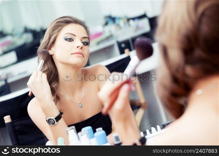 Reflection of young beautiful woman applying her make-up, looking in a mirror
