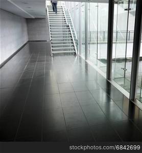 reflections in marble floor with stairs and glass pane of modern architecture and man coming down the stairs
