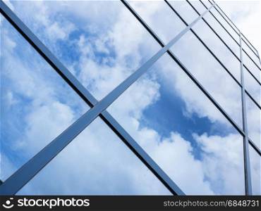 reflections of blue sky and clouds in glass facade of modern office building with diagonal lines