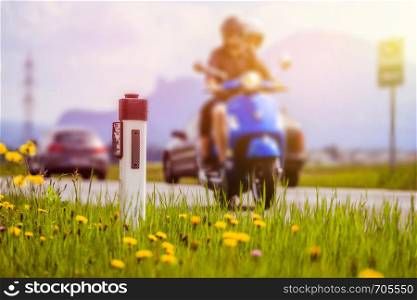 Reflector post and a couple on a motor bike at an idyllic asphalted road in summer, flowers and green grass