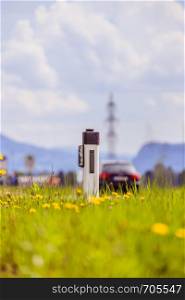 Reflector post and cars at an idyllic asphalted road in summer, flowers and green grass