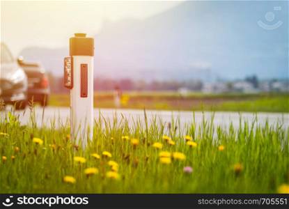 Reflector post and cars at an idyllic asphalted road in summer, flowers and green grass