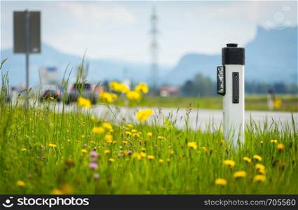 Reflector post at an idyllic asphalted road in summer, flowers and green grass